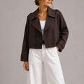 Woman wearing brown cropped trench jacket with double-breasted closure and wide lapels over white trousers