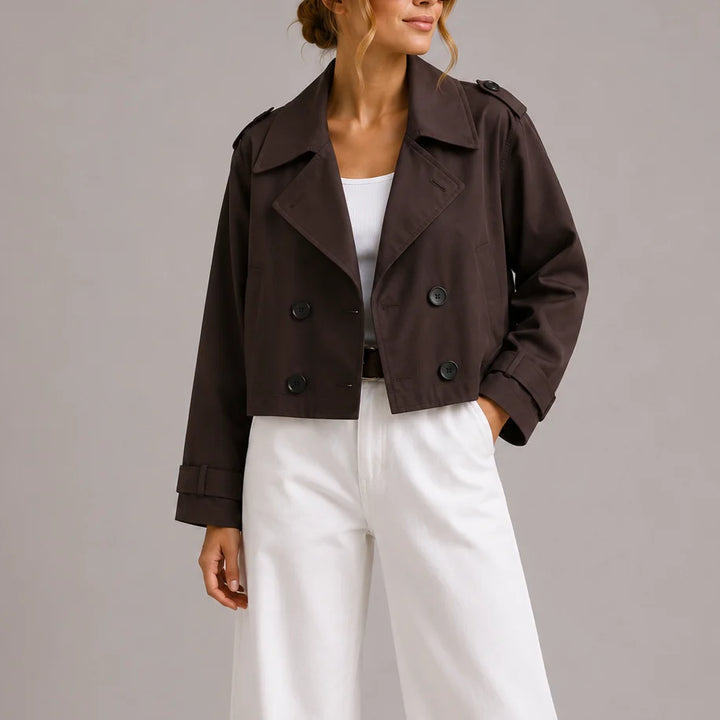 Woman wearing brown cropped trench jacket with double-breasted closure and wide lapels over white trousers