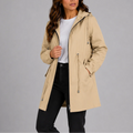 Woman wearing beige hooded rain coat with zip closure and drawstring waist over white tee and black jeans