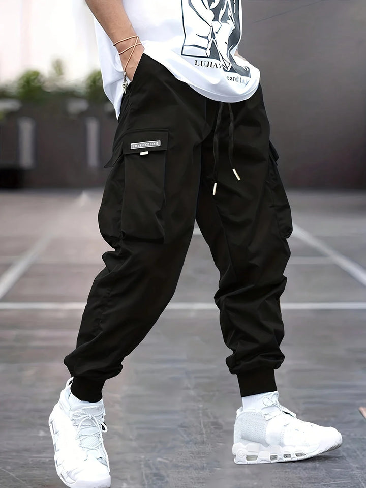 Men's cargo trousers in black with elasticated ankle cuffs and multiple pockets worn with white trainers