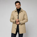 Man wearing beige tailored longline coat with button front closure over black turtleneck and dark trousers