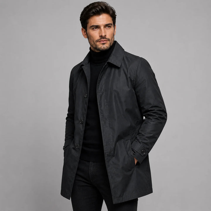 Side profile of man in beige tailored coat displaying longline silhouette and midweight construction over casual layering