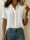 Woman wearing white pleated front blouse with open collar and short sleeves paired with high-waisted jeans