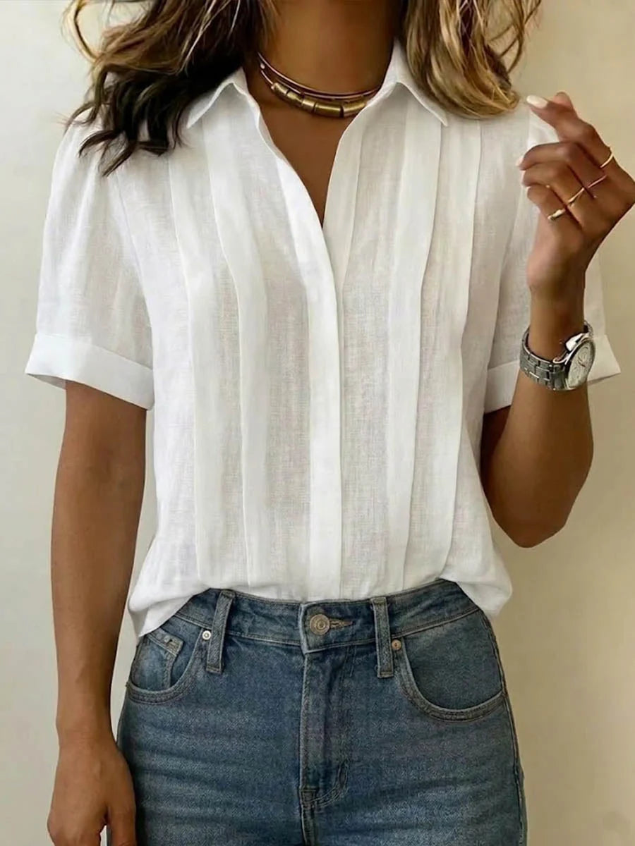 Woman wearing white pleated front blouse with open collar and short sleeves paired with high-waisted jeans