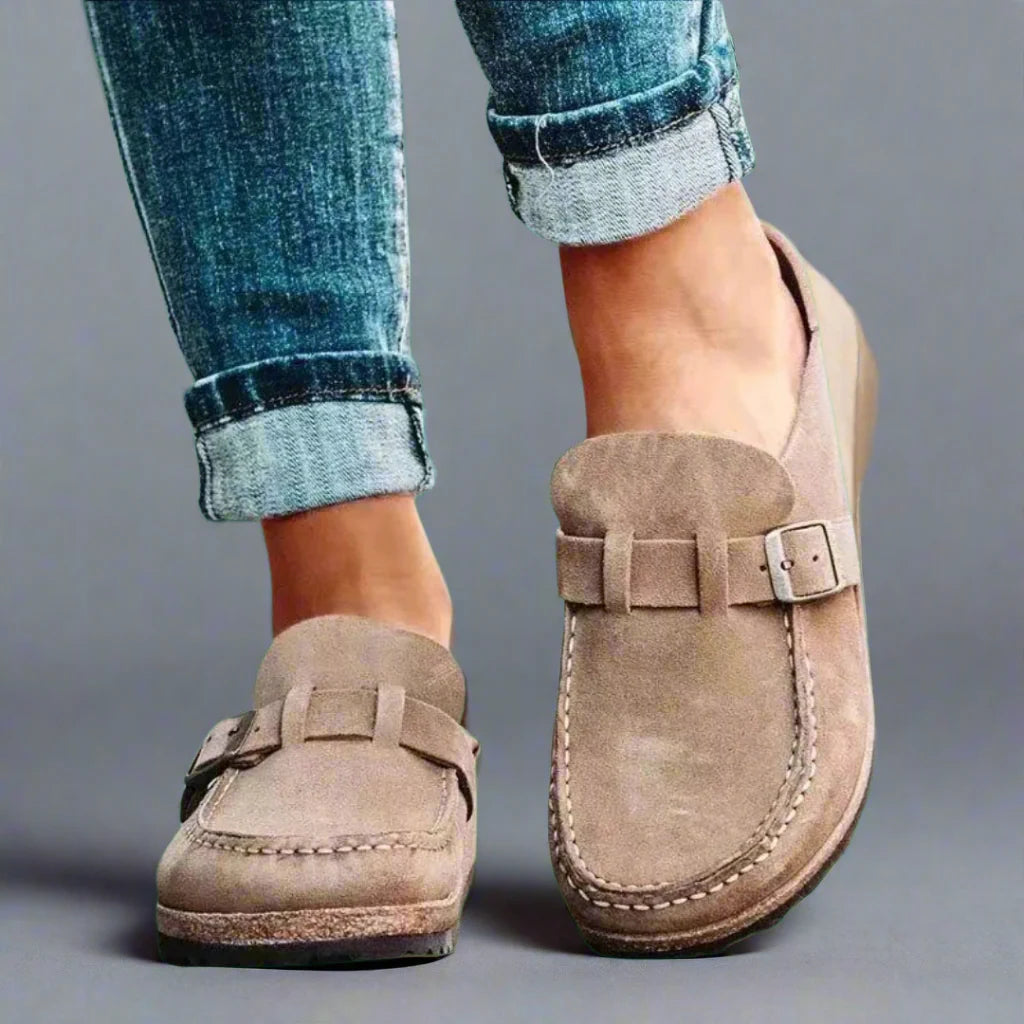 Side angle of women's slip-on mules featuring wide buckle strap and closed-toe design