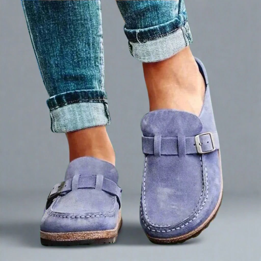 Women's buckle mules paired with rolled-up jeans showing suede-effect upper and adjustable metal buckle
