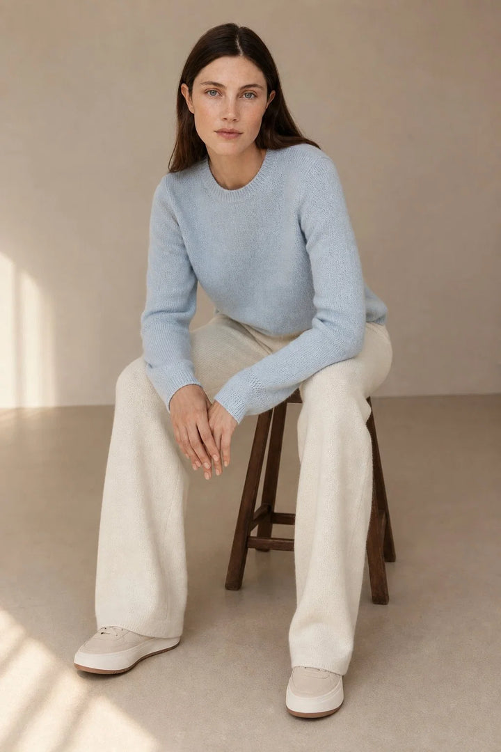 Woman wearing cream wide-leg Merino Pants with high waist and relaxed fit, paired with a light blue knit jumper