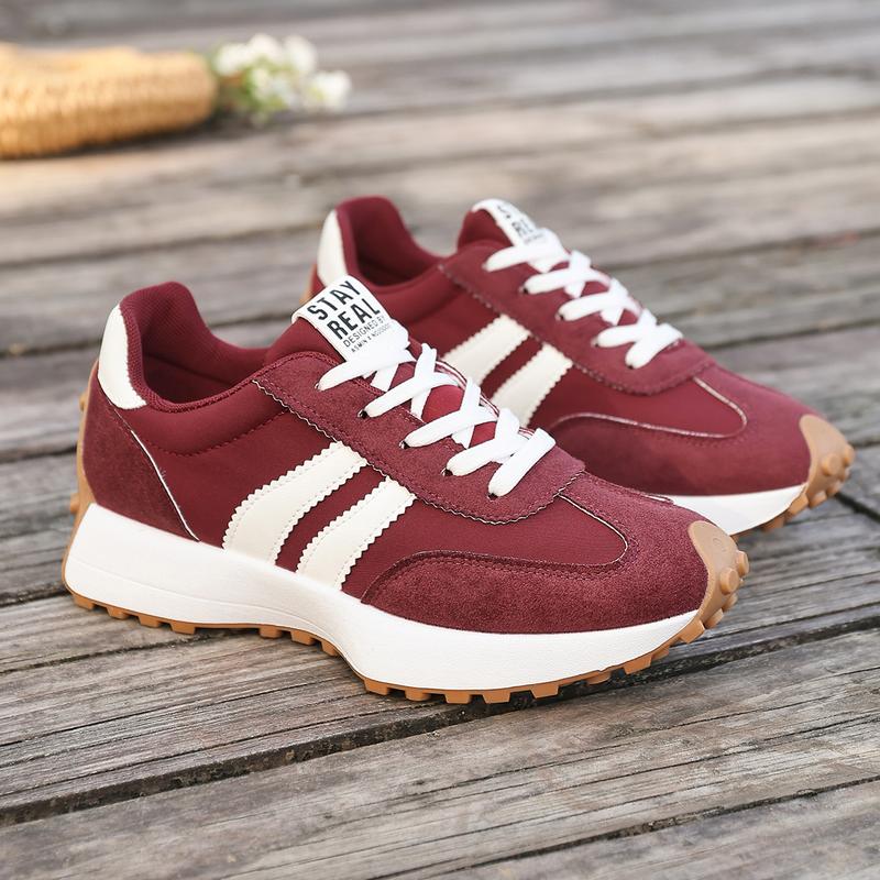 Women's retro running trainers in burgundy with white side stripes and gum rubber outsole on wooden surface