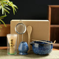 Six-piece matcha tea set with blue ceramic bowl, bamboo whisk, sieve, and spoon on woven mat