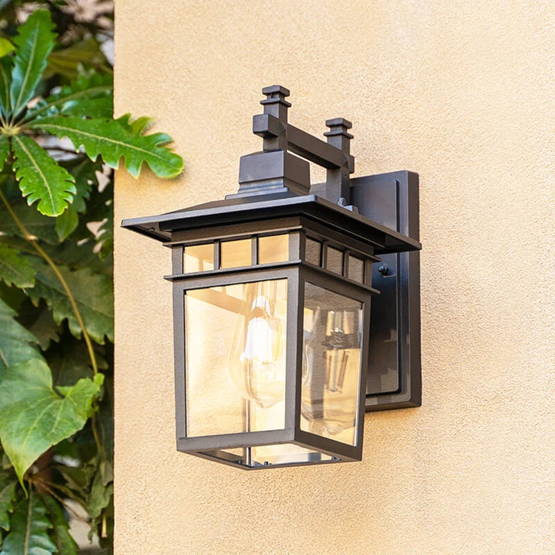 Outdoor lantern wall light mounted on garden wall near greenery