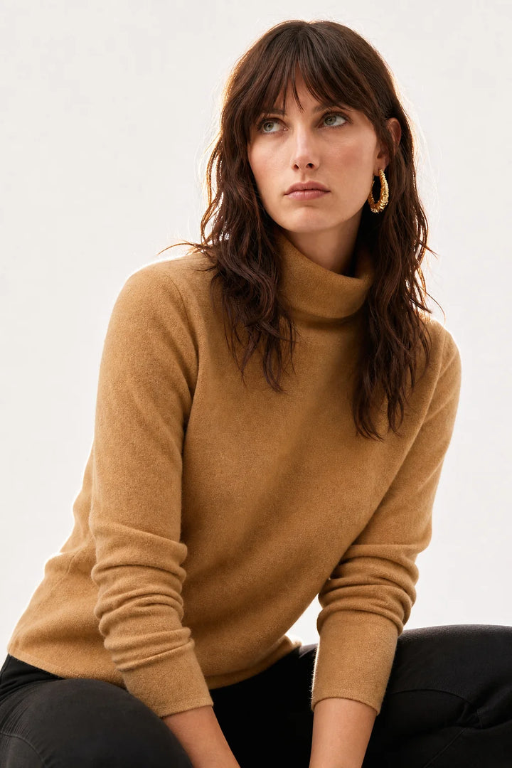 Woman styling a cashmere turtleneck jumper with tailored trousers, showcasing the versatile layering piece