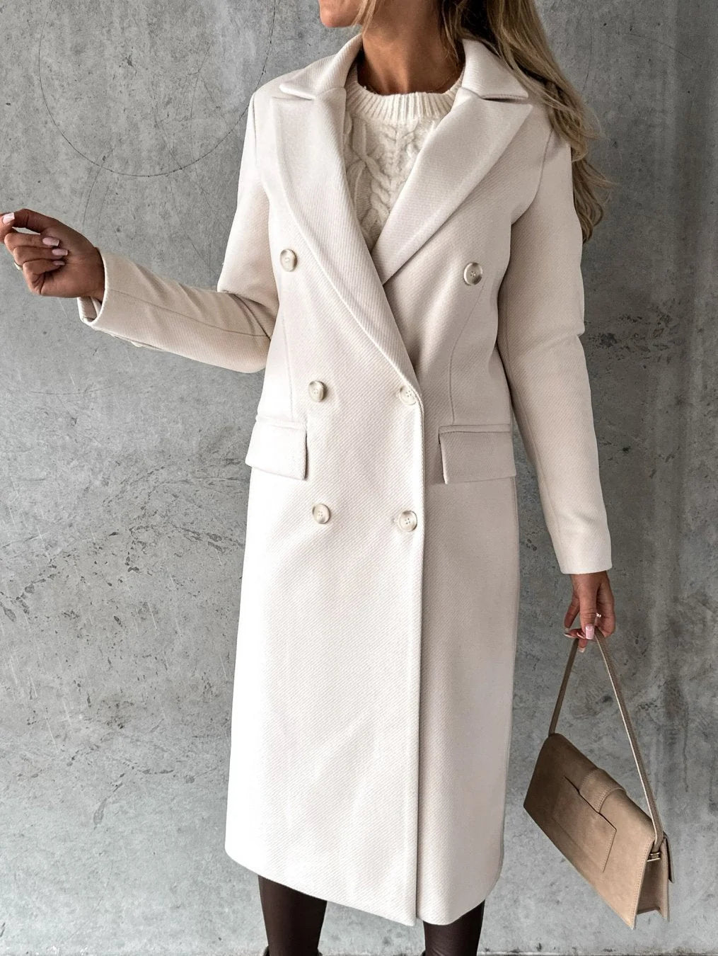 Side profile of women's mid-thigh length coat with tailored shoulders and functional hip pockets over fitted trousers