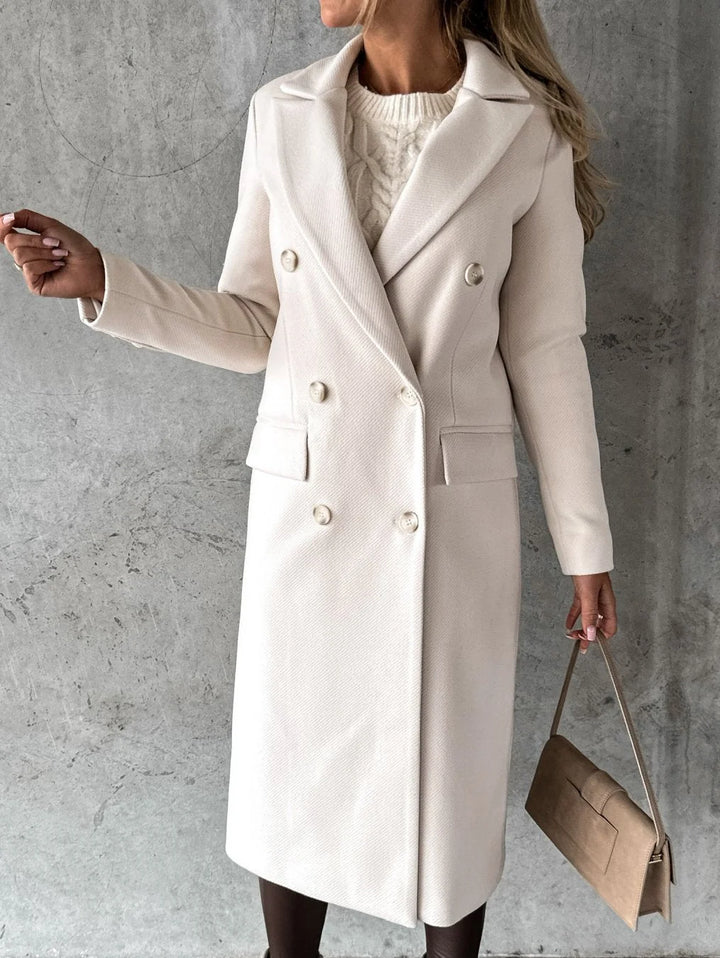 Side profile of women's mid-thigh length coat with tailored shoulders and functional hip pockets over fitted trousers