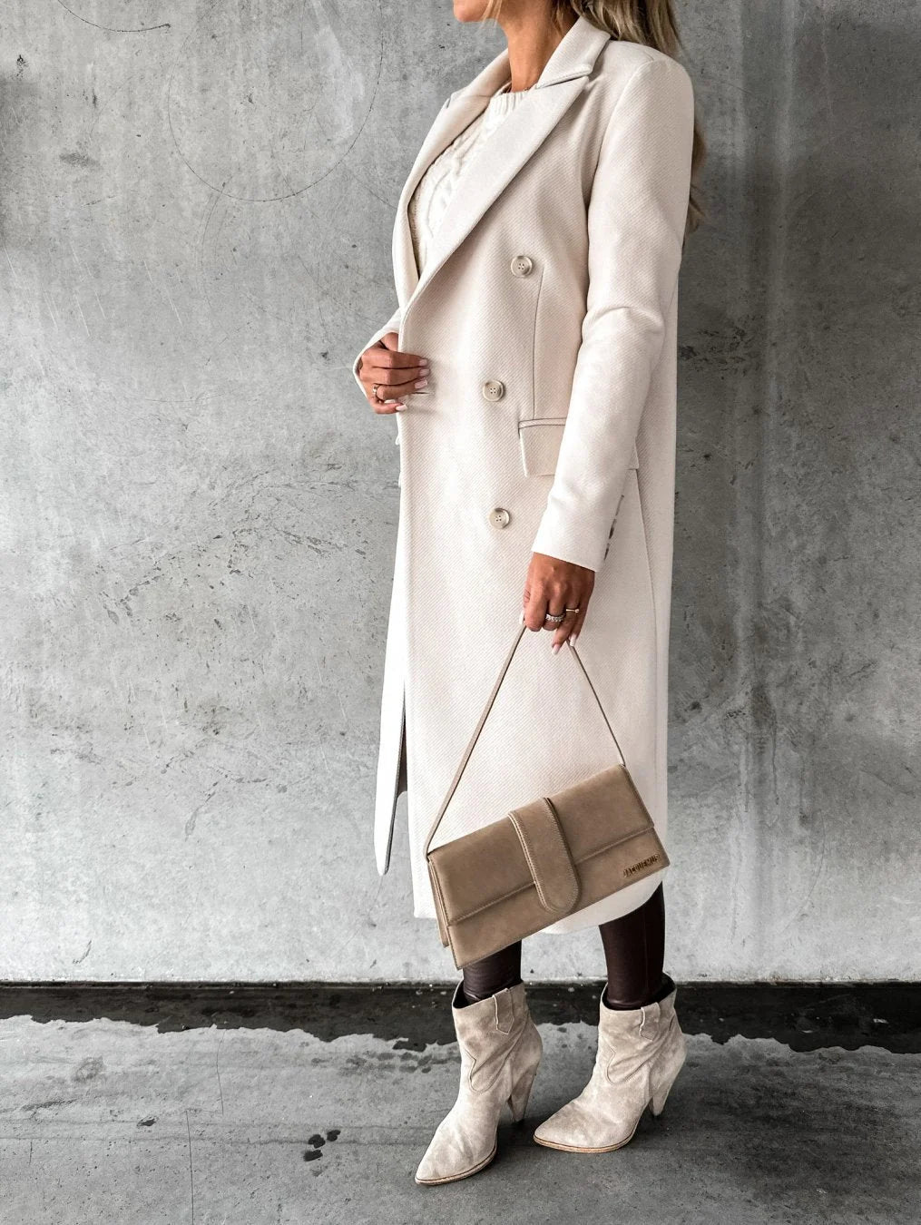 Detail shot of women's longline coat featuring notched collar and double-breasted closure paired with cable knit top