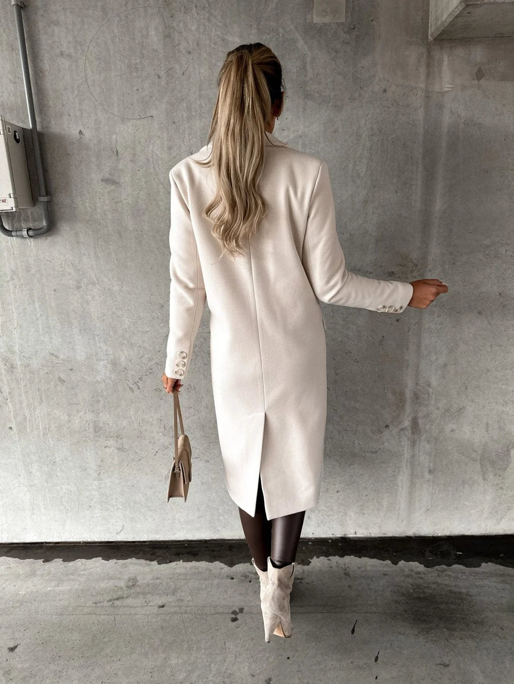 Women's beige longline coat with structured fit and smooth finish, layered over knitwear and leather trousers