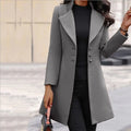 Close-up view of women's long tailored coat showing structured fabric, notch lapels, and decorative button accents.