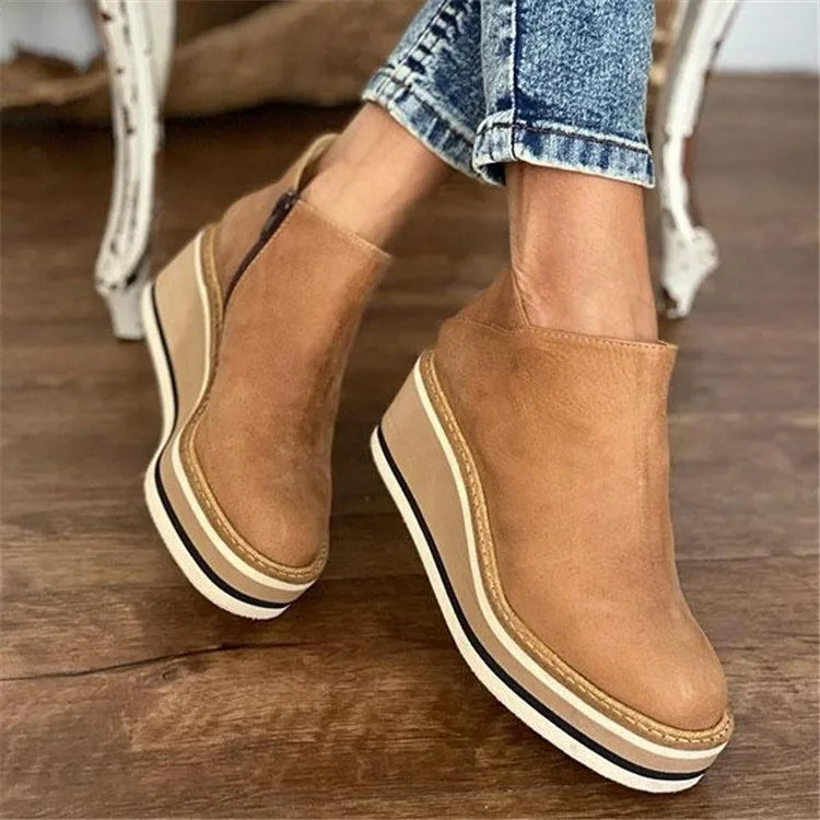 Women's ankle boots in tan with raised sole and side zip closure worn with denim jeans