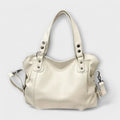 Cream hobo shoulder bag with studded handles and detachable crossbody strap on neutral background
