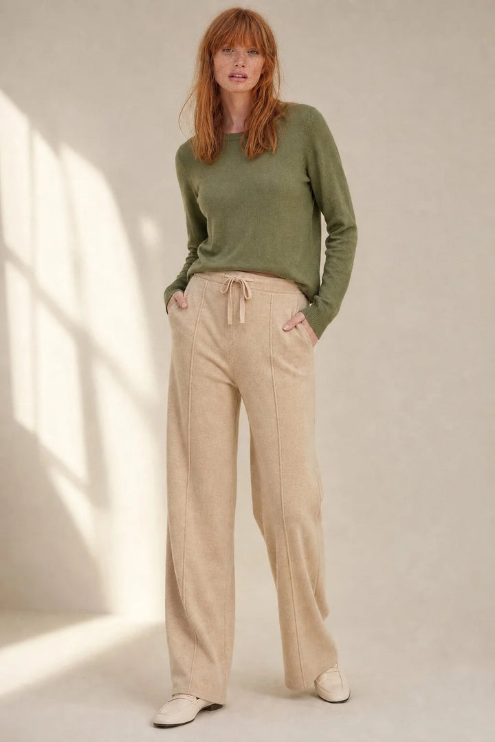 Woman wearing beige wool trousers with wide leg silhouette paired with olive green knit jumper