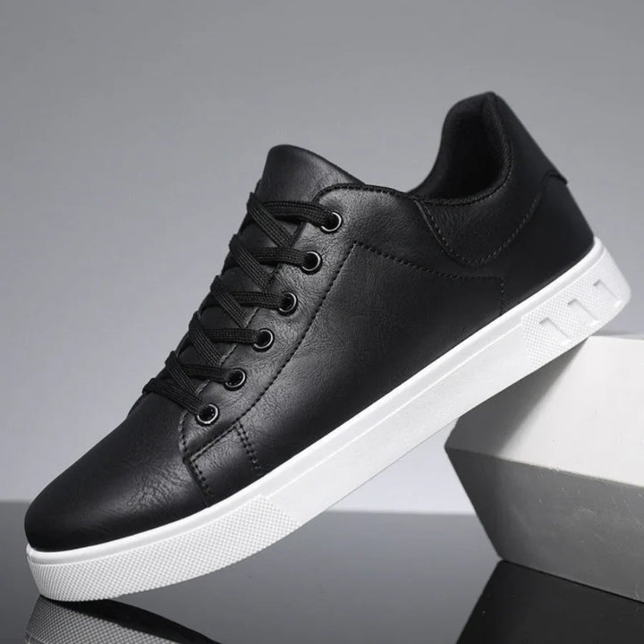 Men's black lace-up trainers with low-top silhouette and contrast white sole displayed on grey surface
