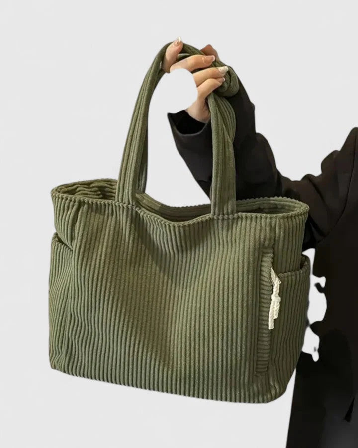 Olive green ribbed corduroy tote bag with dual shoulder straps and exterior side pockets held by model