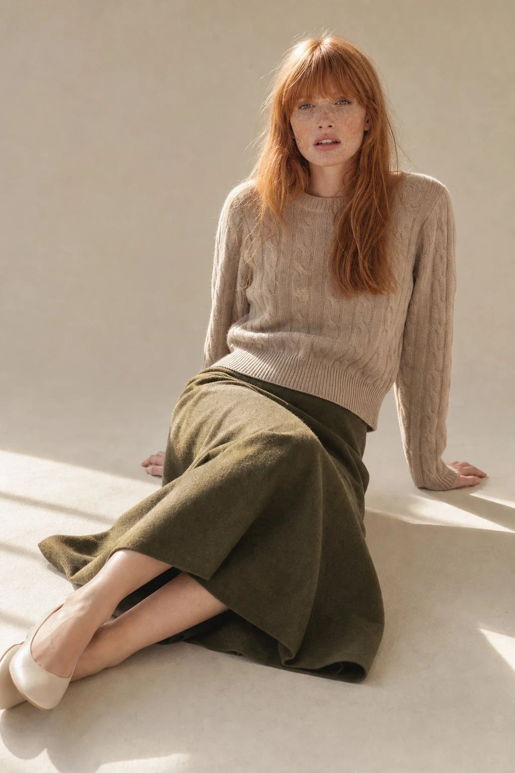 Model wearing olive wool skirt with high waist and relaxed midi length paired with beige cable knit jumper