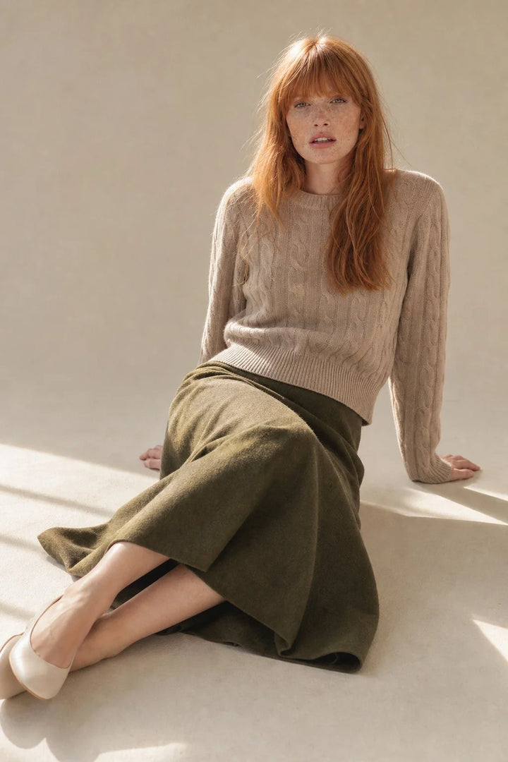 Model wearing olive wool skirt with high waist and relaxed midi length paired with beige cable knit jumper