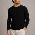 Man wearing black crew neck knit jumper with cream chinos in studio setting