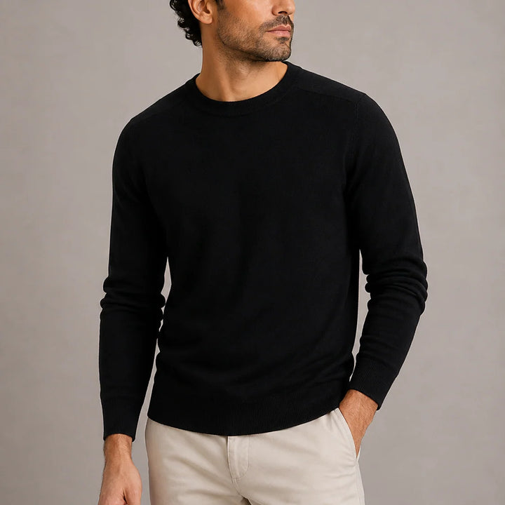 Man wearing black crew neck knit jumper with cream chinos in studio setting