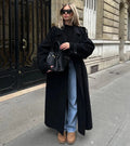 Women's double-breasted trench coat in black with belted waist and long silhouette worn on city street