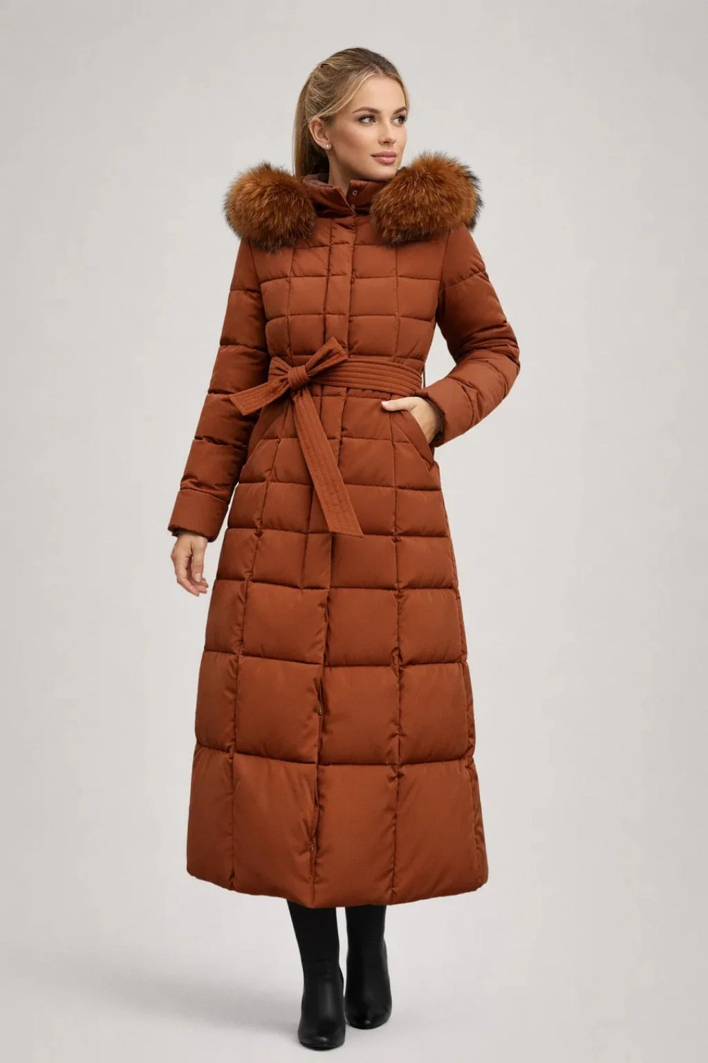 Women's long puffer coat in rust brown with faux fur-trimmed hood and belted waist, full-length quilted design