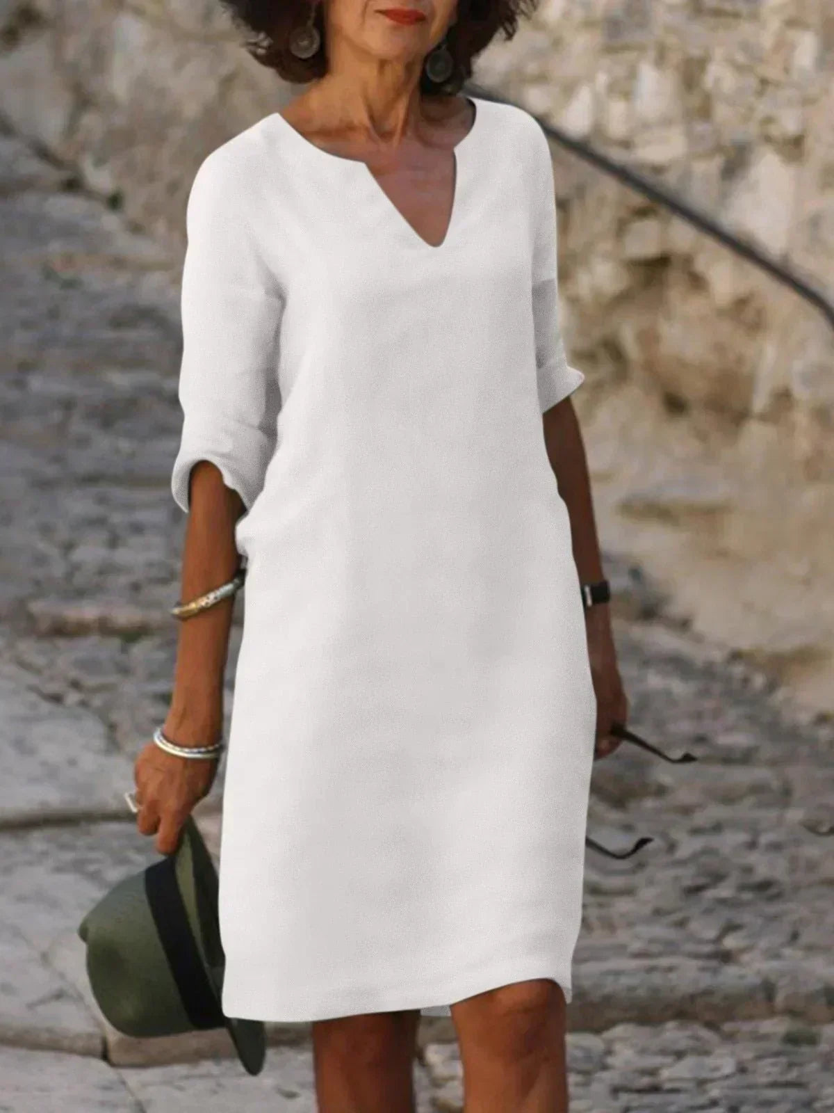 Woman wearing black v-neck dress with roll-tab sleeves paired with casual accessories by water