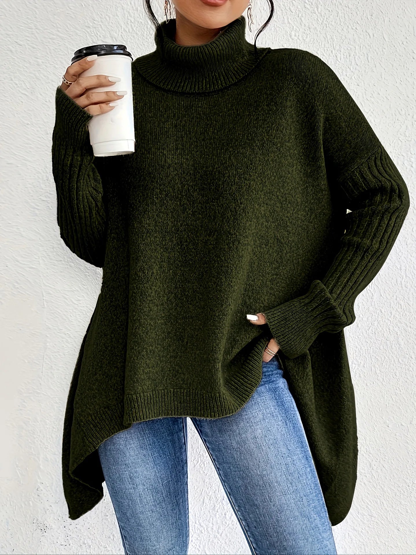 Woman wearing dark olive green oversized turtleneck jumper with relaxed fit and high-low hem paired with denim jeans