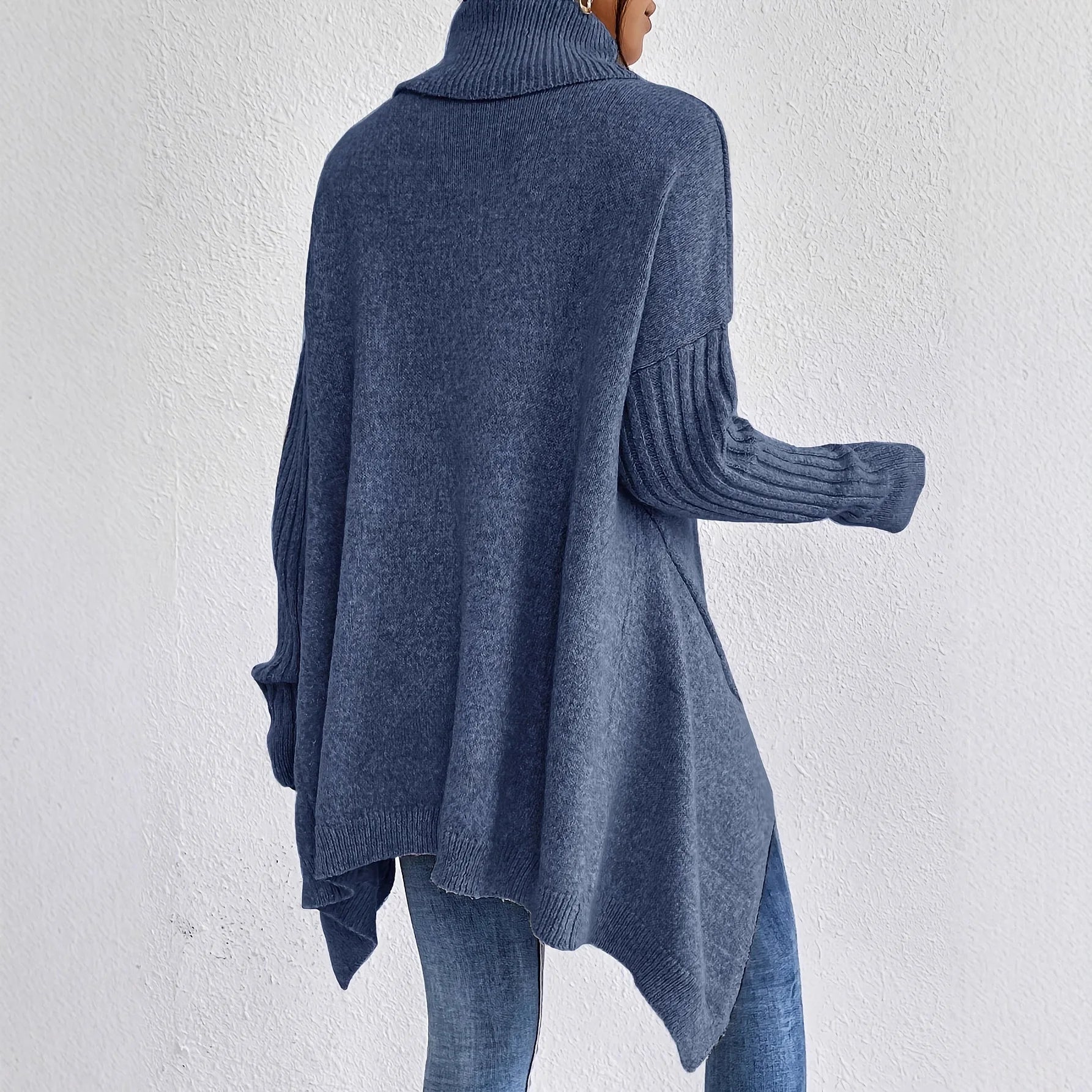 Side angle of oversized turtleneck jumper displaying drop-shoulder sleeves and curved hemline drape on model