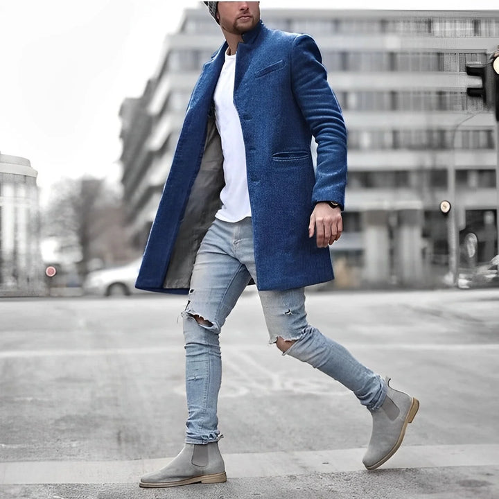 Mid-length men's overcoat with stand collar layered over white tee and distressed jeans