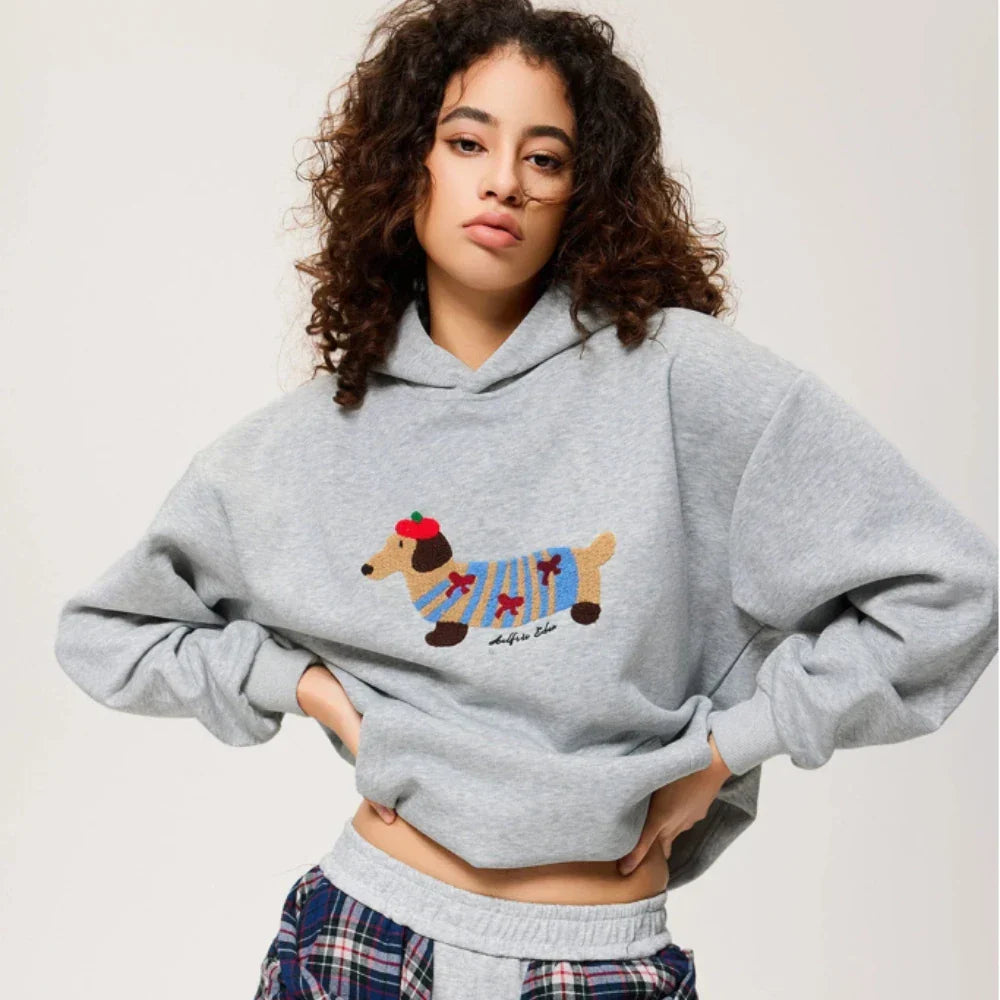 Model wearing grey embroidered dachshund hoodie with plaid shirt tied at waist over joggers