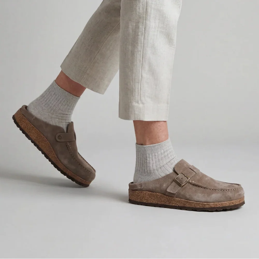 Women's suede clogs with adjustable buckle strap and cork footbed worn with beige trousers